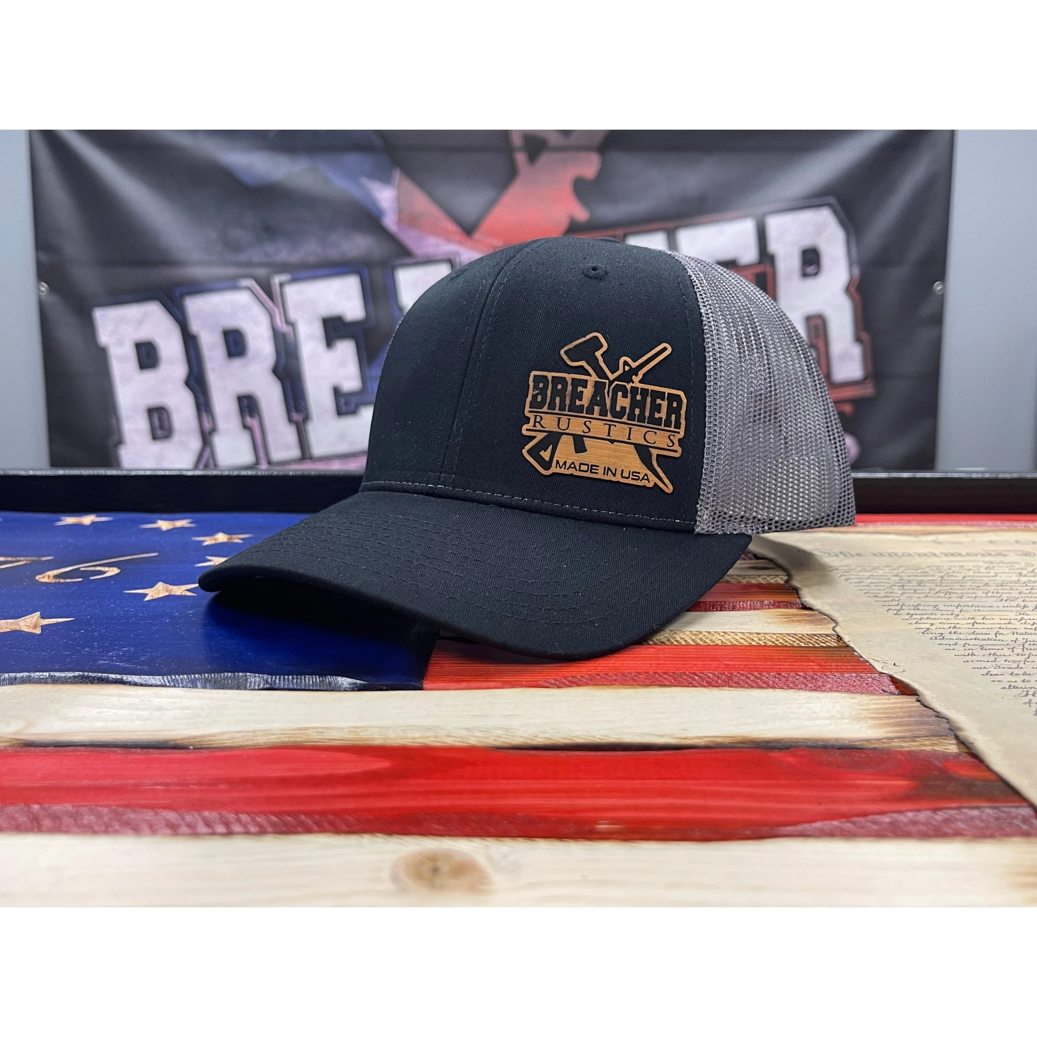 Breacher Rustics black trucker hat with grey mesh back and leather patch logo. Structured, six-panel, low-profile with snapback closure.