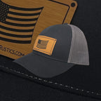 Breacher Rustics charcoal cotton trucker hat with grey mesh back and a bamboo leather patch featuring a draped American flag.
