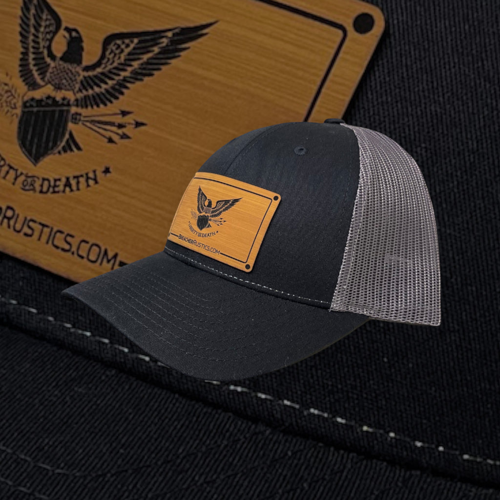 Breacher Rustics black trucker hat with grey mesh back and a bamboo leather patch featuring an eagle emblem and "Liberty or Death" text.