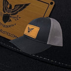 Breacher Rustics black trucker hat with grey mesh back and a bamboo leather patch featuring an eagle emblem and "Liberty or Death" text.