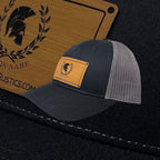 Breacher Rustics Molon Labe trucker hat with bamboo leather patch, dark grey cotton front, and grey mesh back. Adjustable snapback.