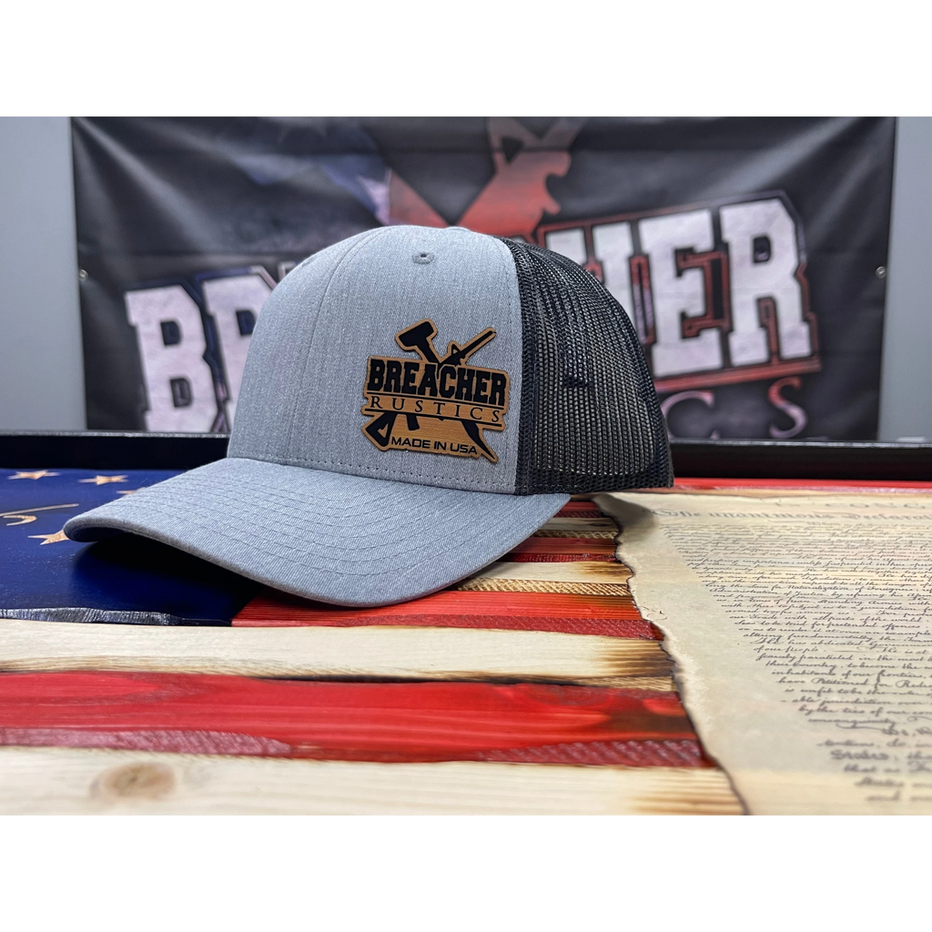 Breacher Rustics silver trucker hat with black mesh back and leather patch logo. Six-panel, low-profile, pre-curved visor, snapback closure.