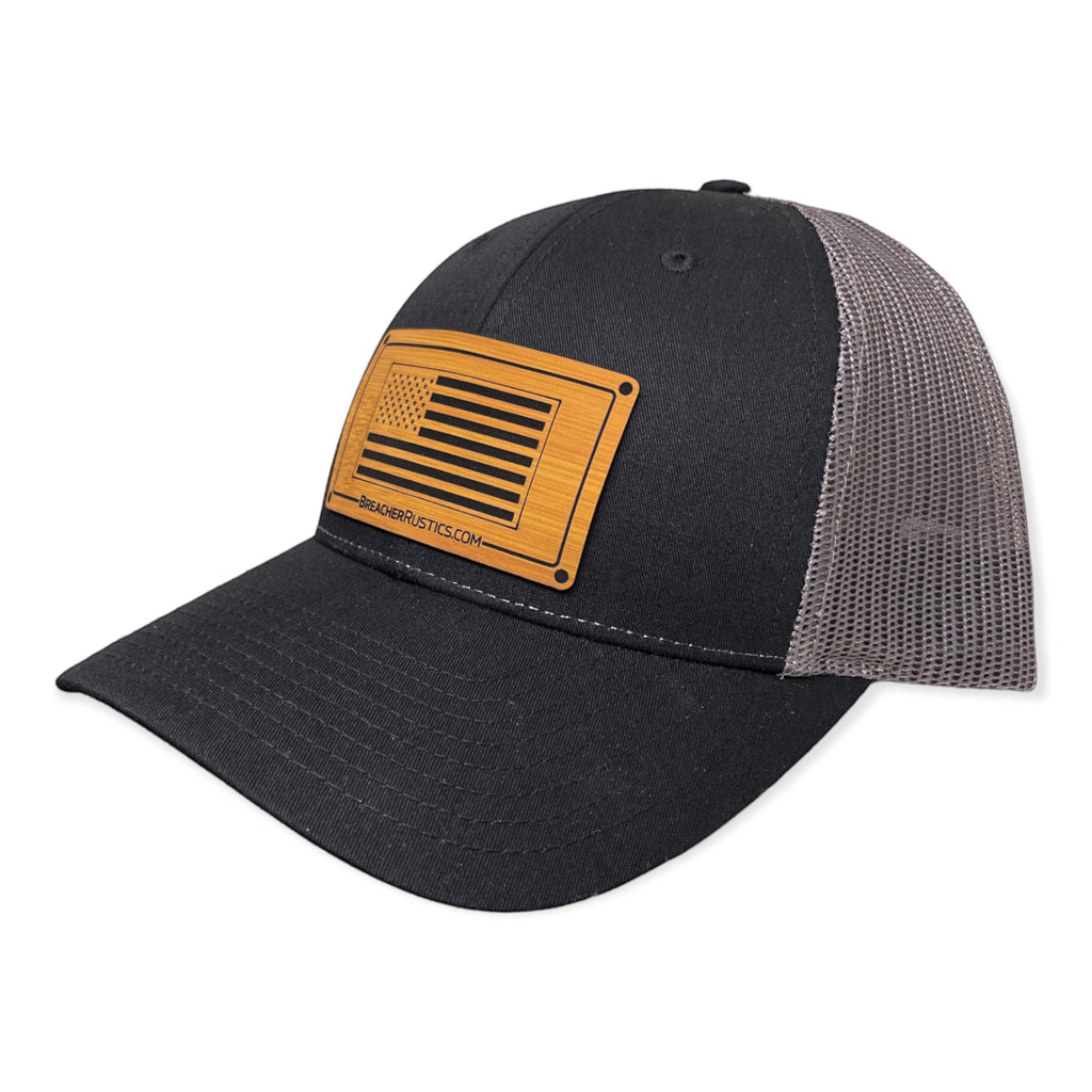 Breacher Rustics black cotton-nylon trucker hat with a wooden USA flag patch and grey mesh back. Adjustable snapback.