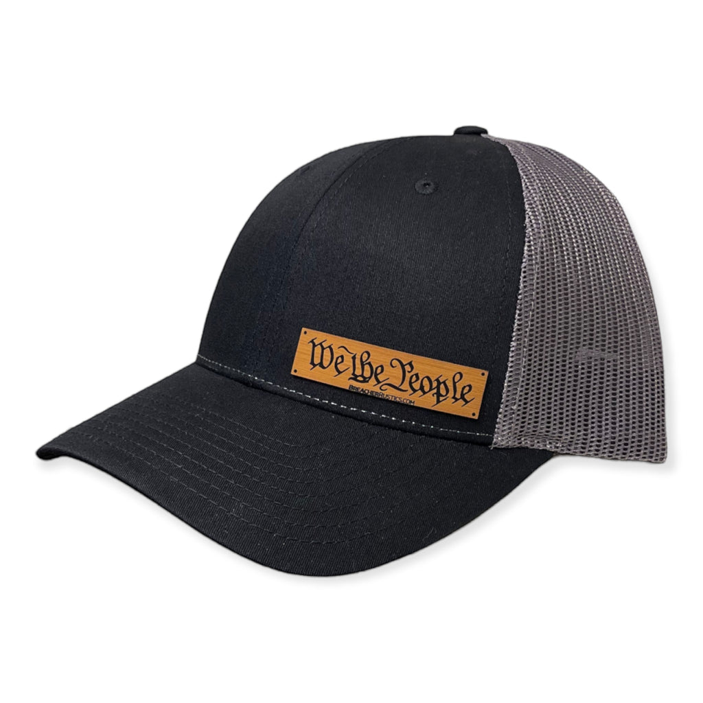 Breacher Rustics black cotton trucker hat with grey mesh back and a bamboo leather patch that says "We The People".