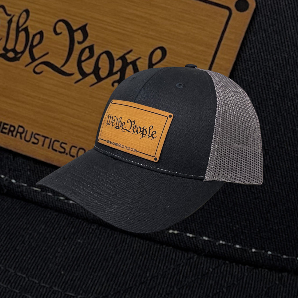 Breacher Rustics black trucker hat with "We The People" bamboo leather patch and grey mesh back. Adjustable snapback.