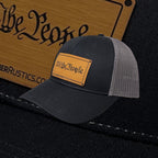 Breacher Rustics black trucker hat with "We The People" bamboo leather patch and grey mesh back. Adjustable snapback.